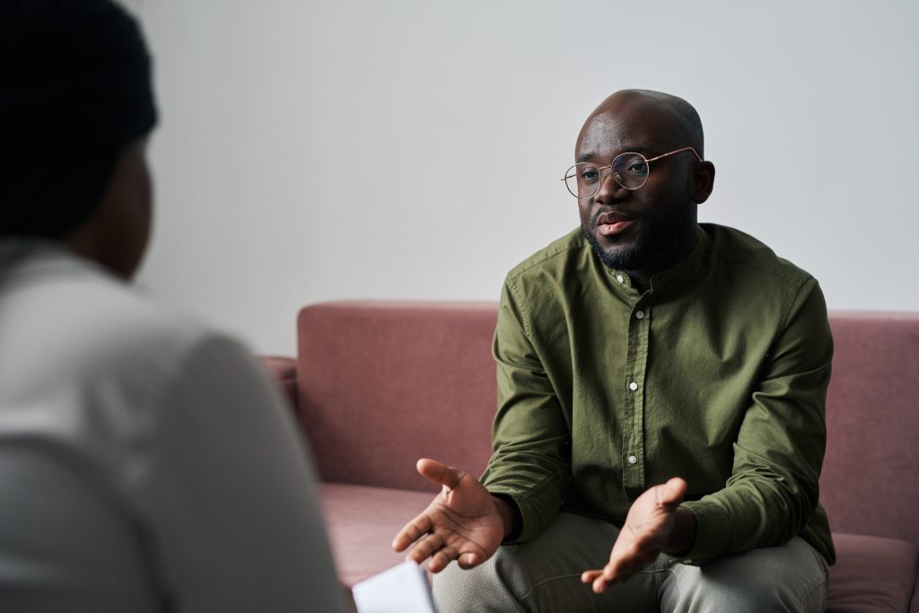 Young black man in casualwear sitting on couch during talk with psychoanalyst