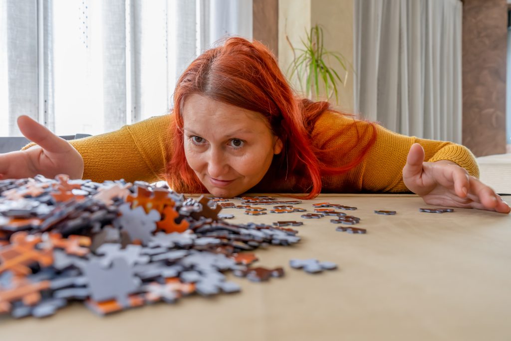 Beautiful redhead woman in a yellow sweater doing a puzzle in the living room at home